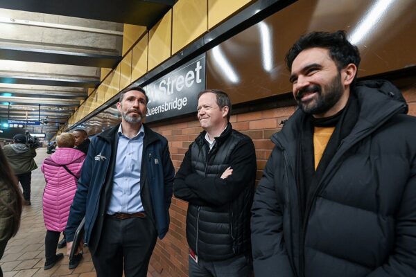 Zohran Mamdani smiles alongside supporters in a New York subway station near a 63rd Street-Queensbridge campaign sign.