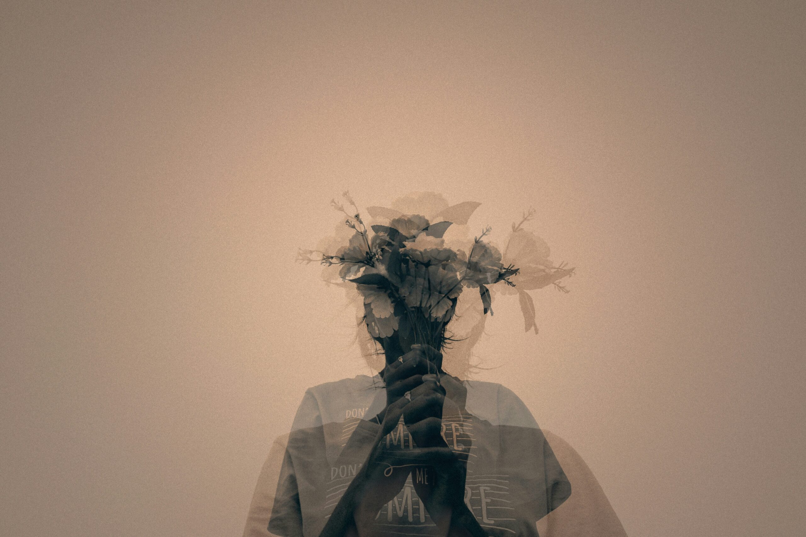 Double exposure image of a person holding a bouquet of flowers over their face, creating a ghostly, layered effect against a monochrome background, symbolizing the fragmentation of perception in schizophrenia.