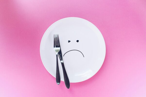 Empty white plate with a sad face drawn on it and utensils resting on top, symbolizing the emotional impact of hunger.