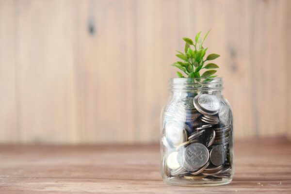 A clear glass jar filled with coins topped by a small growing plant, symbolizing wealth accumulation and growth.