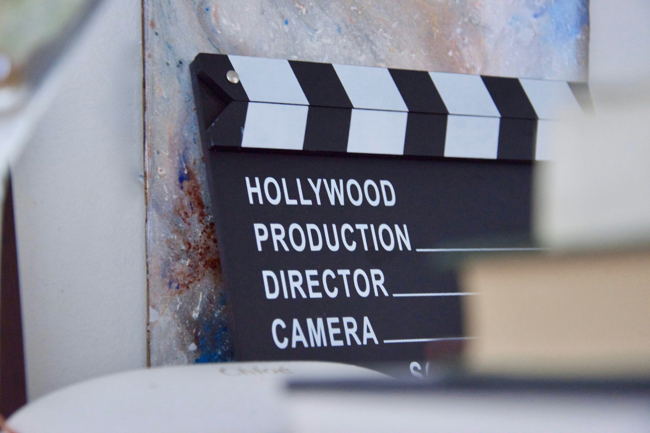Black and white film clapperboard with “Hollywood Production” text, leaning against a textured wall