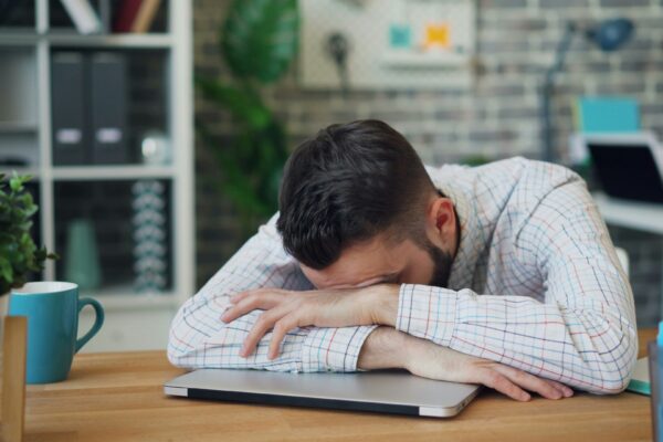 Stress, fatigue, burnout, all makes this man in a white shirt in an office lay his head down on his laptop