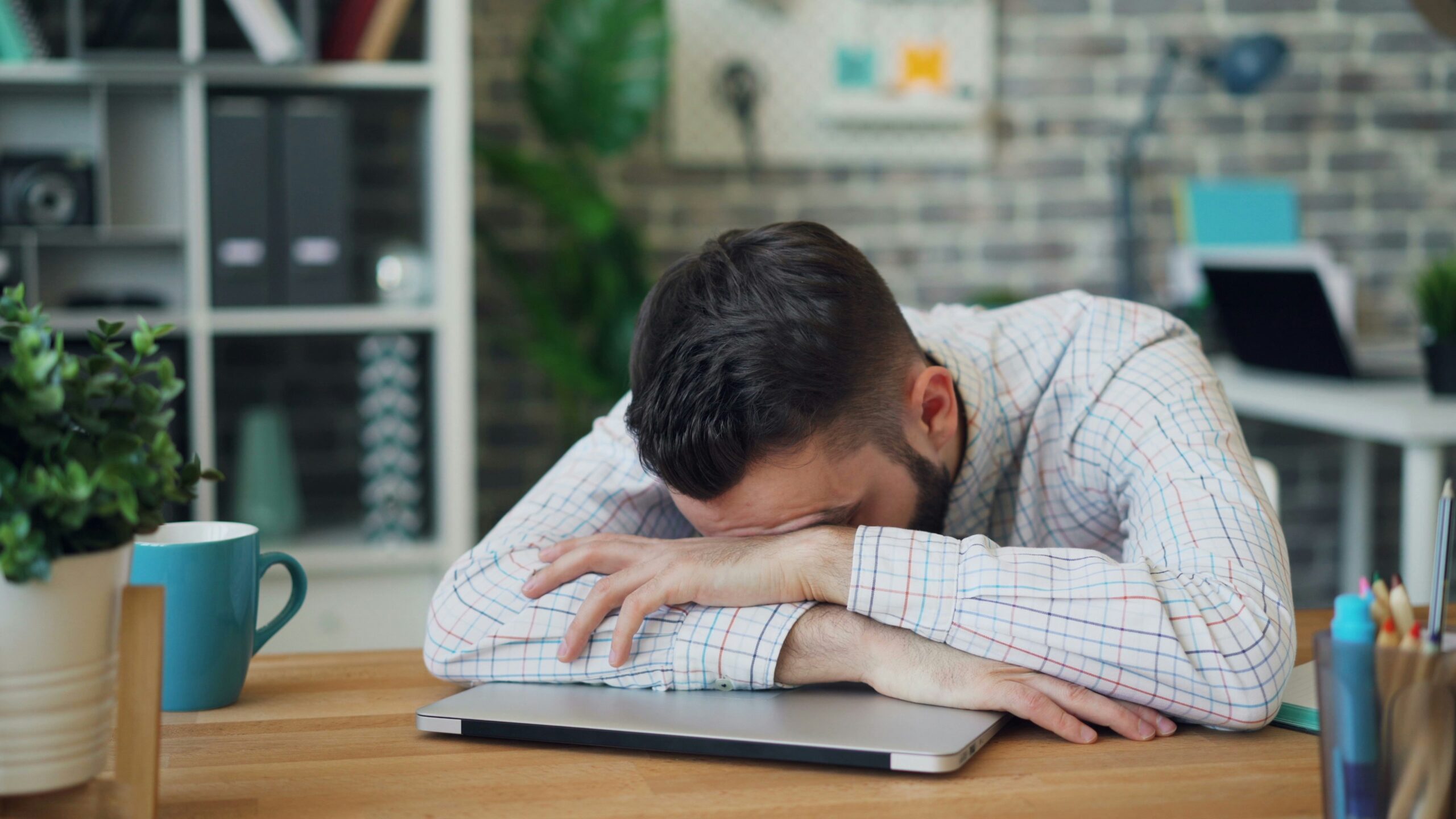 Stress, fatigue, burnout, all makes this man in a white shirt in an office lay his head down on his laptop