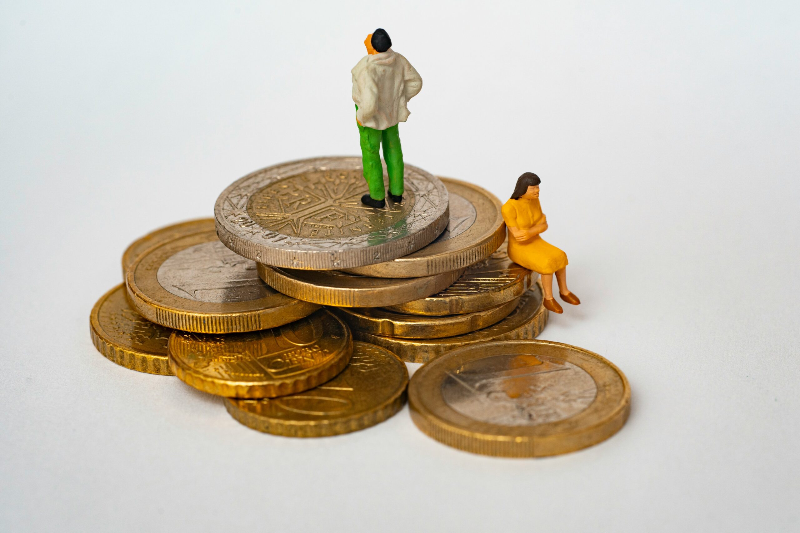 Income Inequality metaphor. A tiny clay man and a tiny clay woman sit on some coins