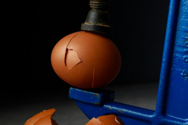 Egg in a clamp with shells under pressure. a Metaphor for Why the Surge in Warehouse Fires and Public Anger Feels Predictable.