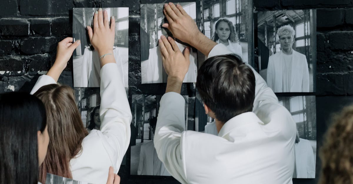 Adults in white suits arranging black and white photos on a brick wall. Showing humans who might be replaceable.