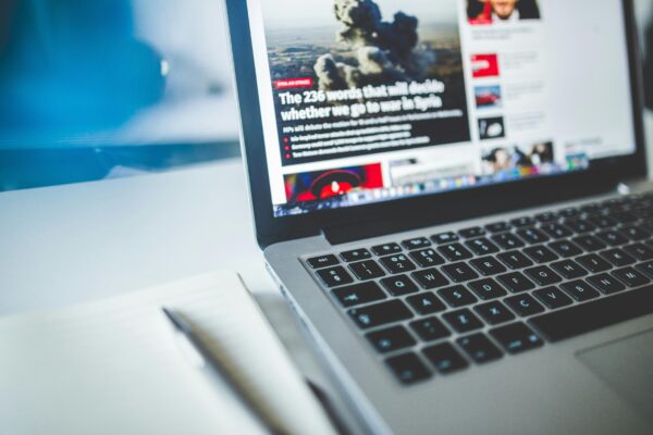 Open laptop displaying an online news article on a desk with a notebook nearby. Preparing us to talk about news media ownership.