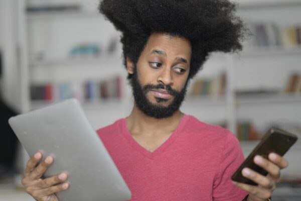A man with afro hair multitasking with a tablet and smartphone indoors, showcasing technology use.