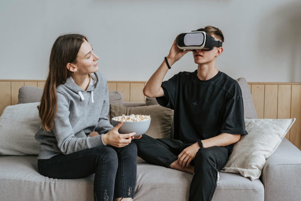 A couple enjoying virtual reality and sharing popcorn on a cozy sofa indoors. But they cannot have a Shared Reality when only one is seeing inside a headset.