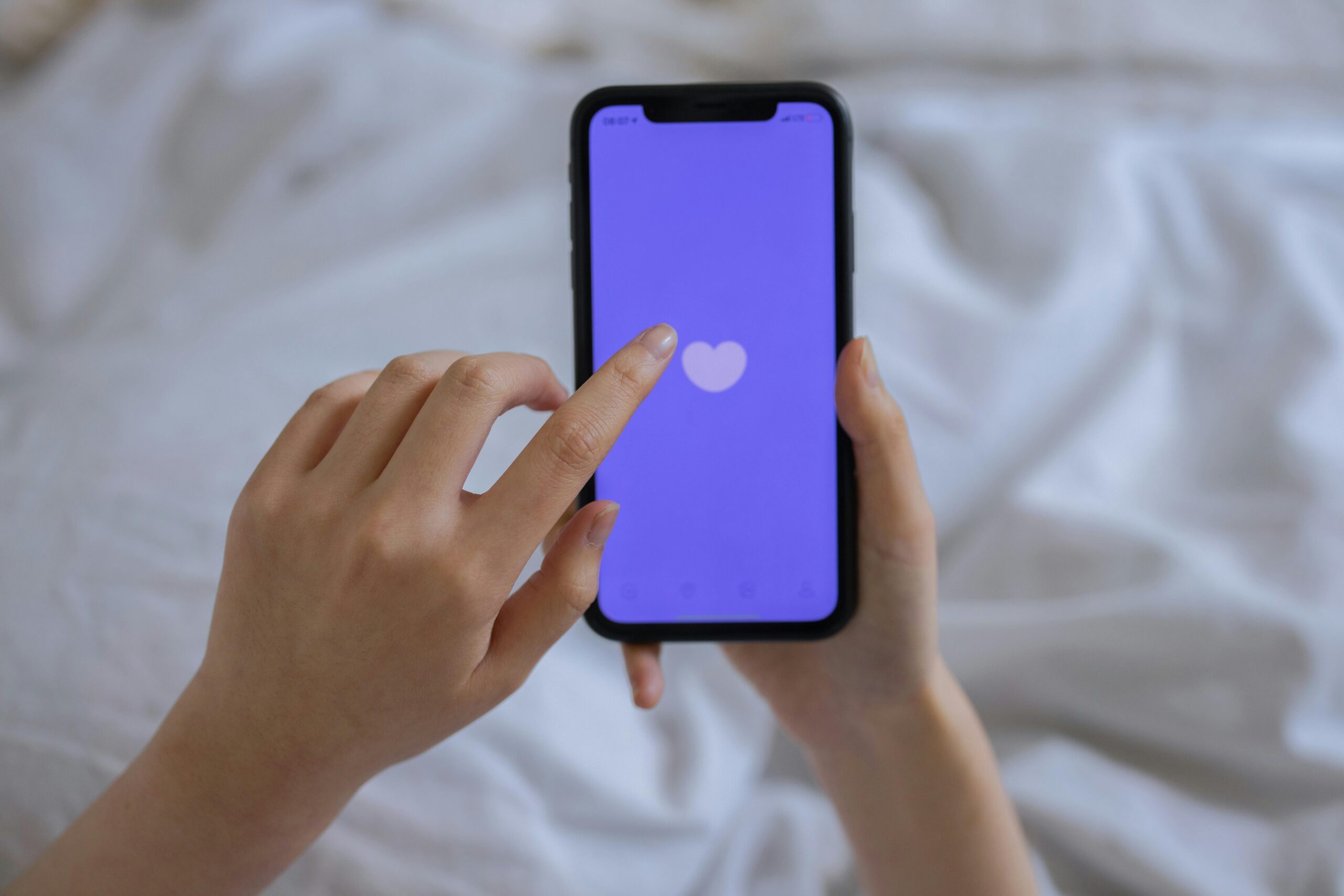 Close-up of hands using a smartphone with a heart icon on screen, representing technology and connection. An image to talk about AI and Dating.