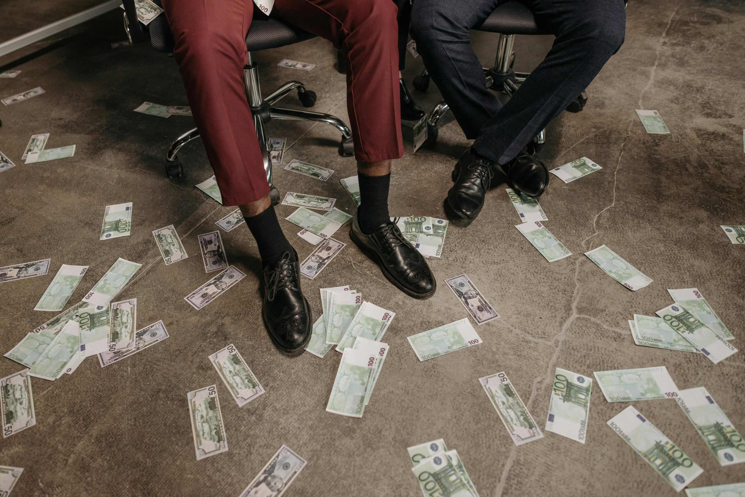 Two people in an office with euro banknotes scattered on the floor, showcasing a financial theme of those with wealth getting away with crime.