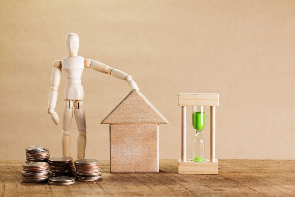Wooden mannequin with house model, coins, and hourglass symbolizing financial planning and time poverty.