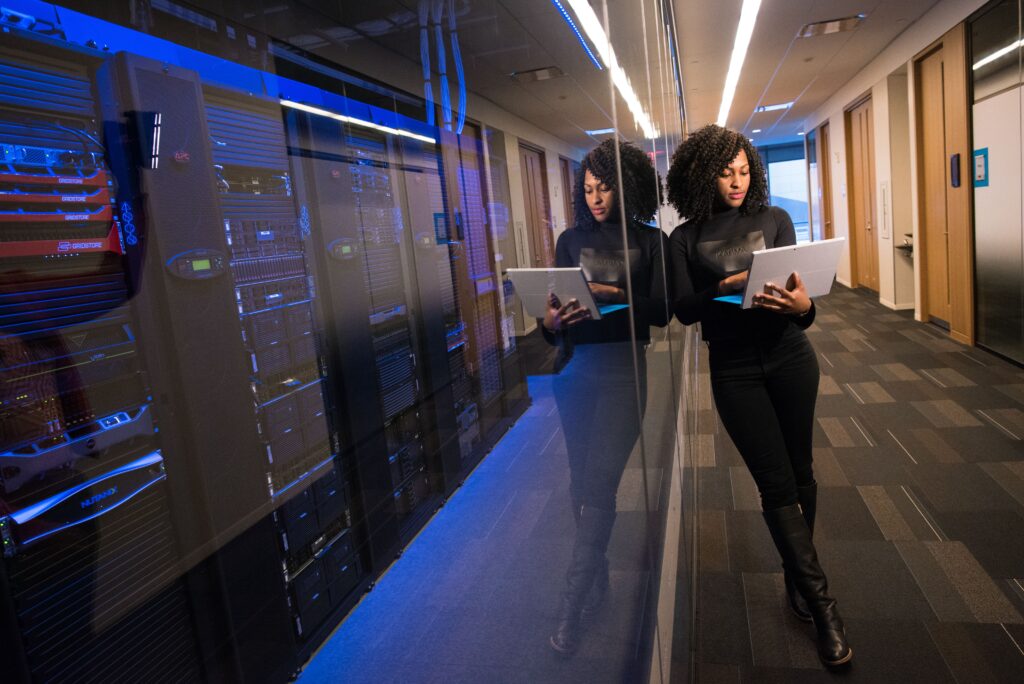 A woman using a laptop navigating a contemporary data centers with mirrored servers.