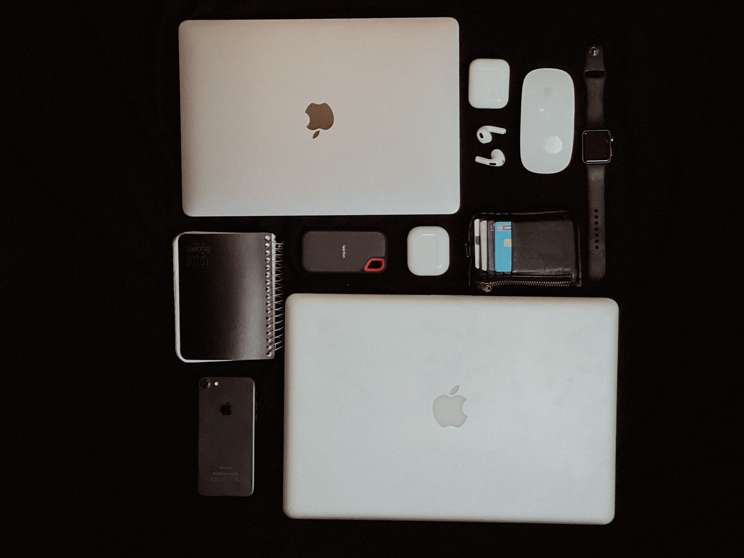 Top view of modern apple electronics including laptops, smartphone, and accessories on a dark background.