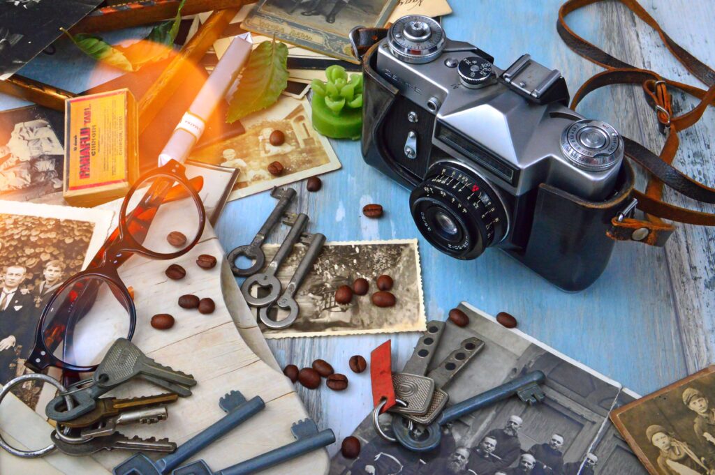 A nostalgic flat lay featuring a vintage camera, eyewear, keys, and old photographs. Items that suggest memory.