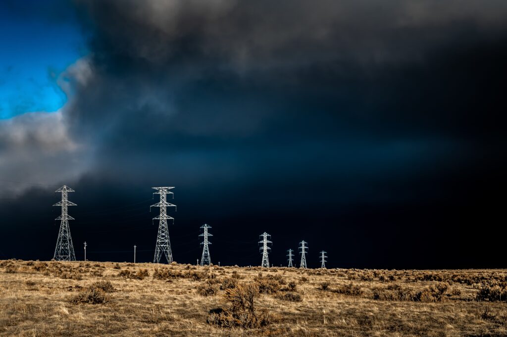 Power lines standing tall against dark storm clouds with a dramatic sky and open field.