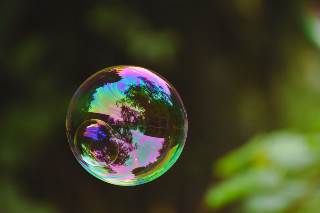 A vibrant iridescent soap bubble floating gently outdoors with natural reflections. A symbol of the AI bubble.