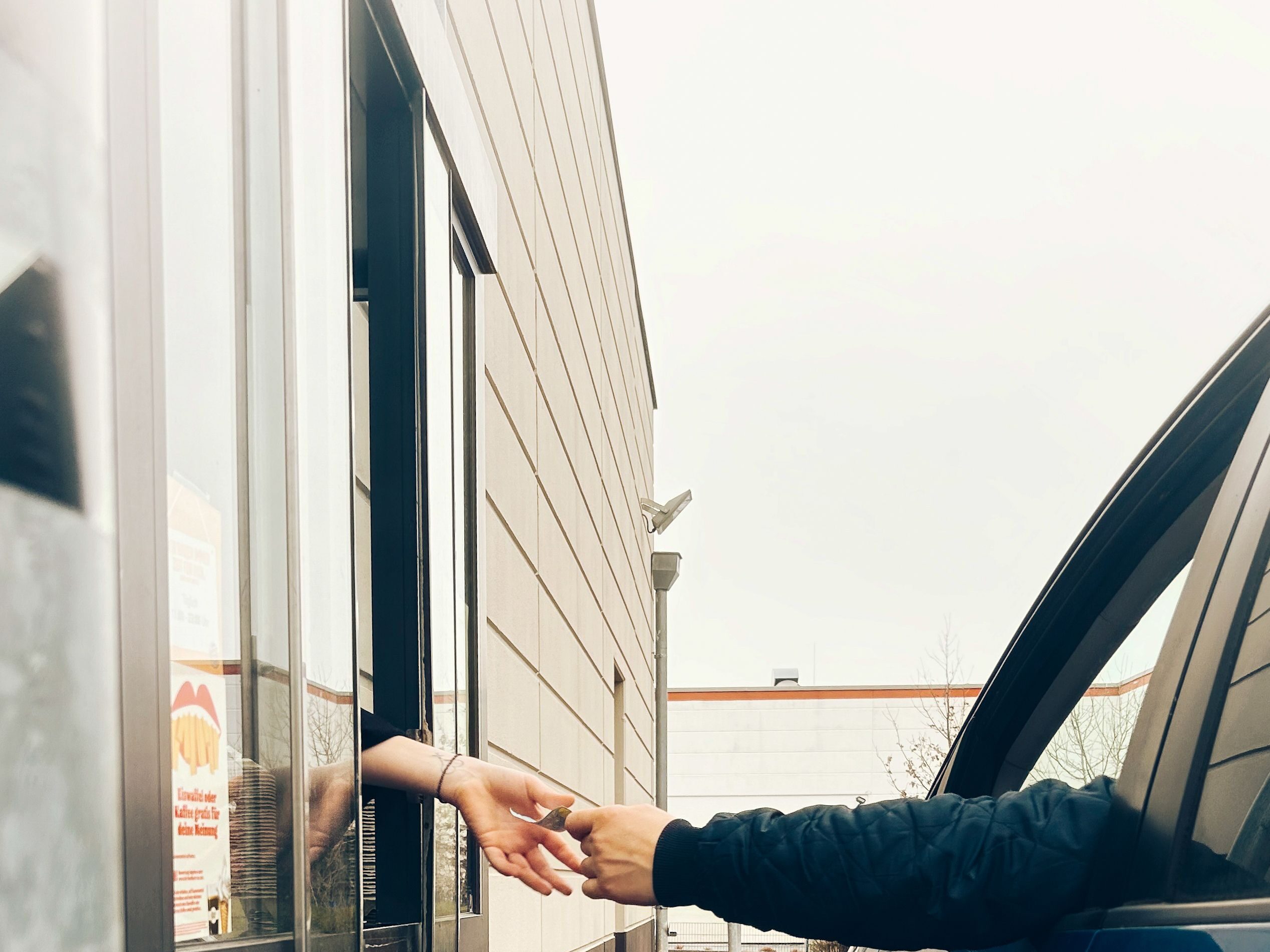 A friendly drive-thru interaction with hands exchanging items at a fast-food window.