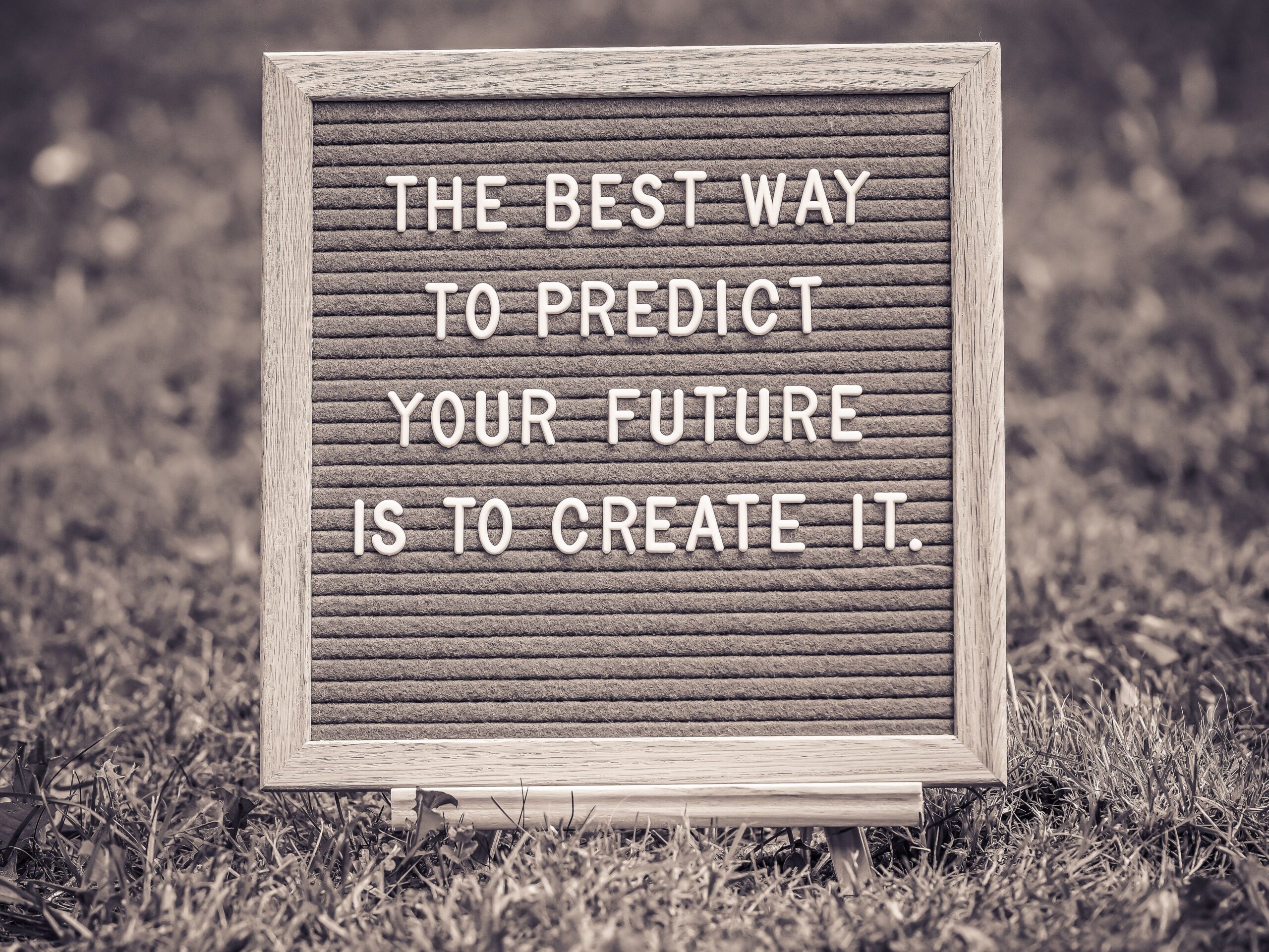 Letter board with motivational quote on grass background in black and white. This is a quote that say "The best way to predict your future is to create it." It is all about Predictions.