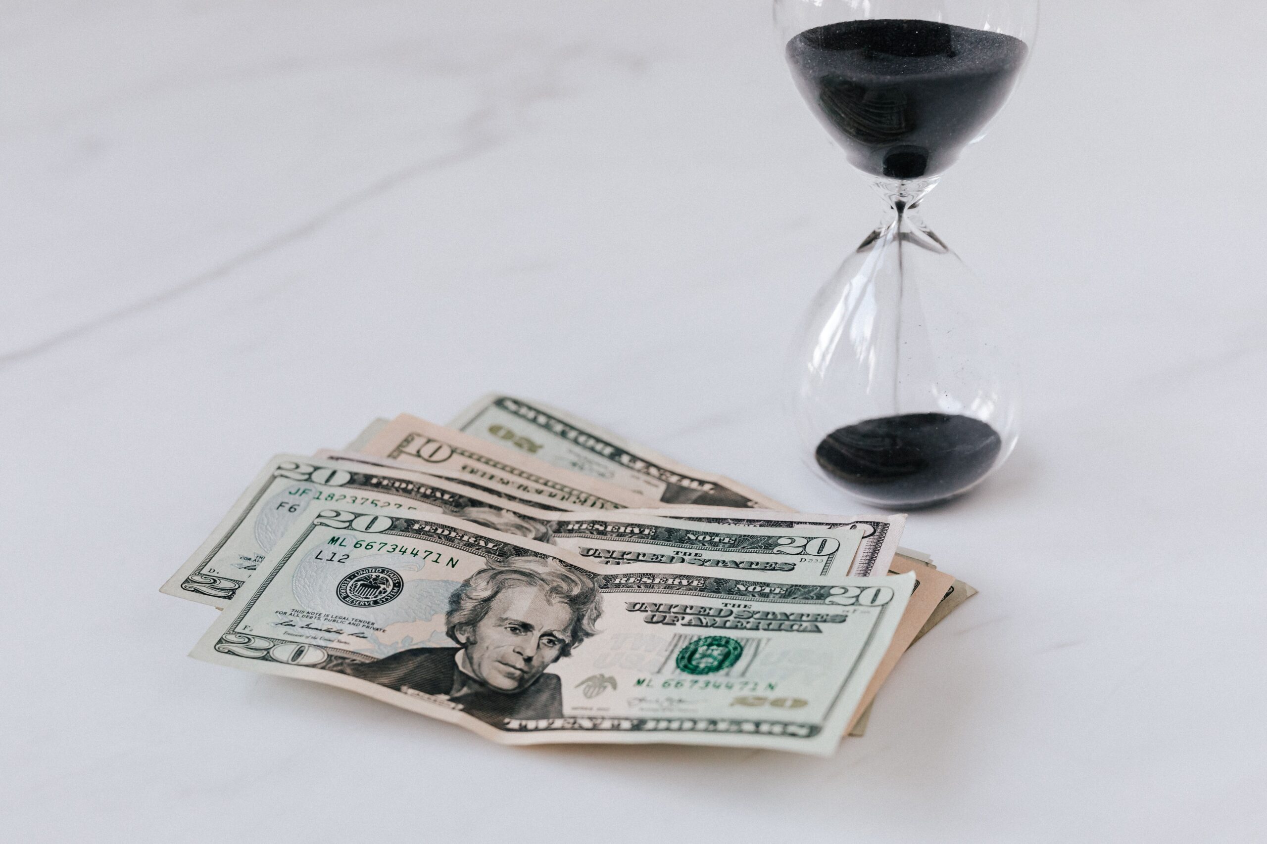 From above of transparent glass with black sand on white table and pile of paper money with image of president, this represents time poverty.