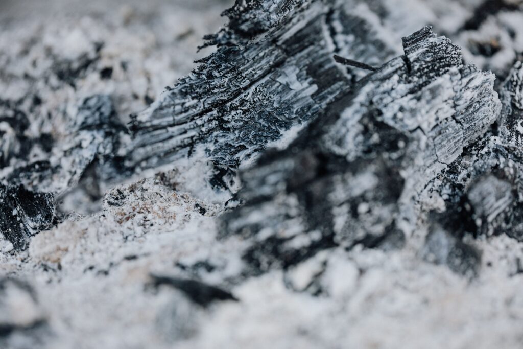 Macro shot showcasing the intricate textures of burned charcoal surrounded by white ash.
