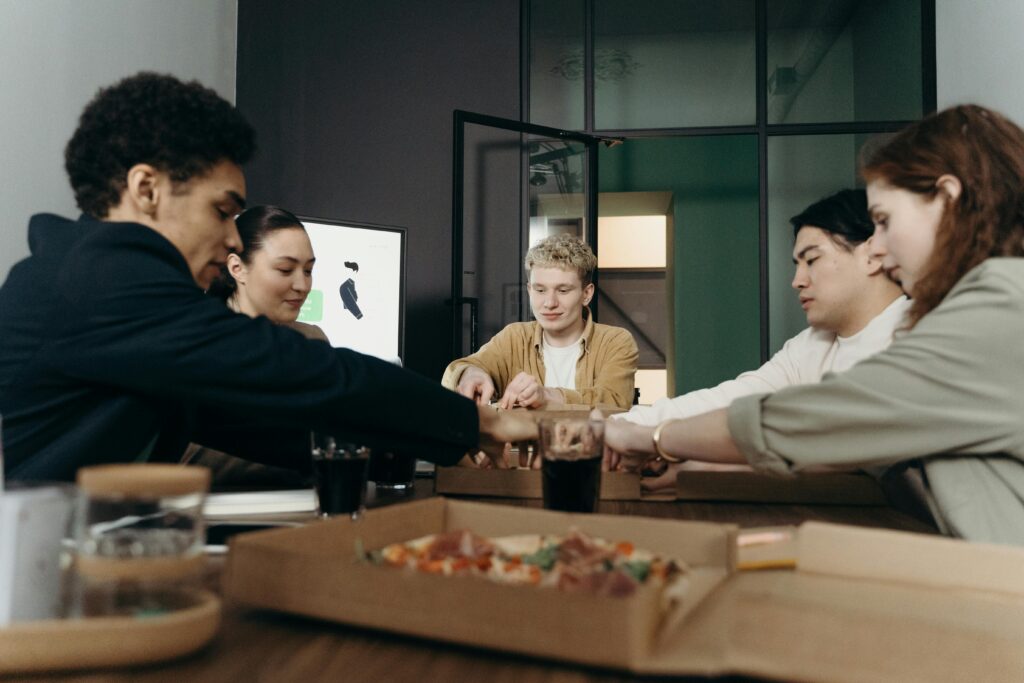 A diverse group of colleagues enjoying a pizza lunch break in a modern office setting as a community.