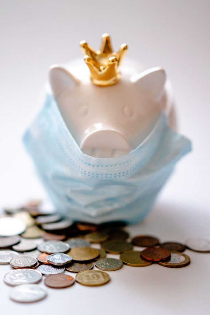 Money box with crown and protective mask among coins representing concept of saving money during COVID pandemic