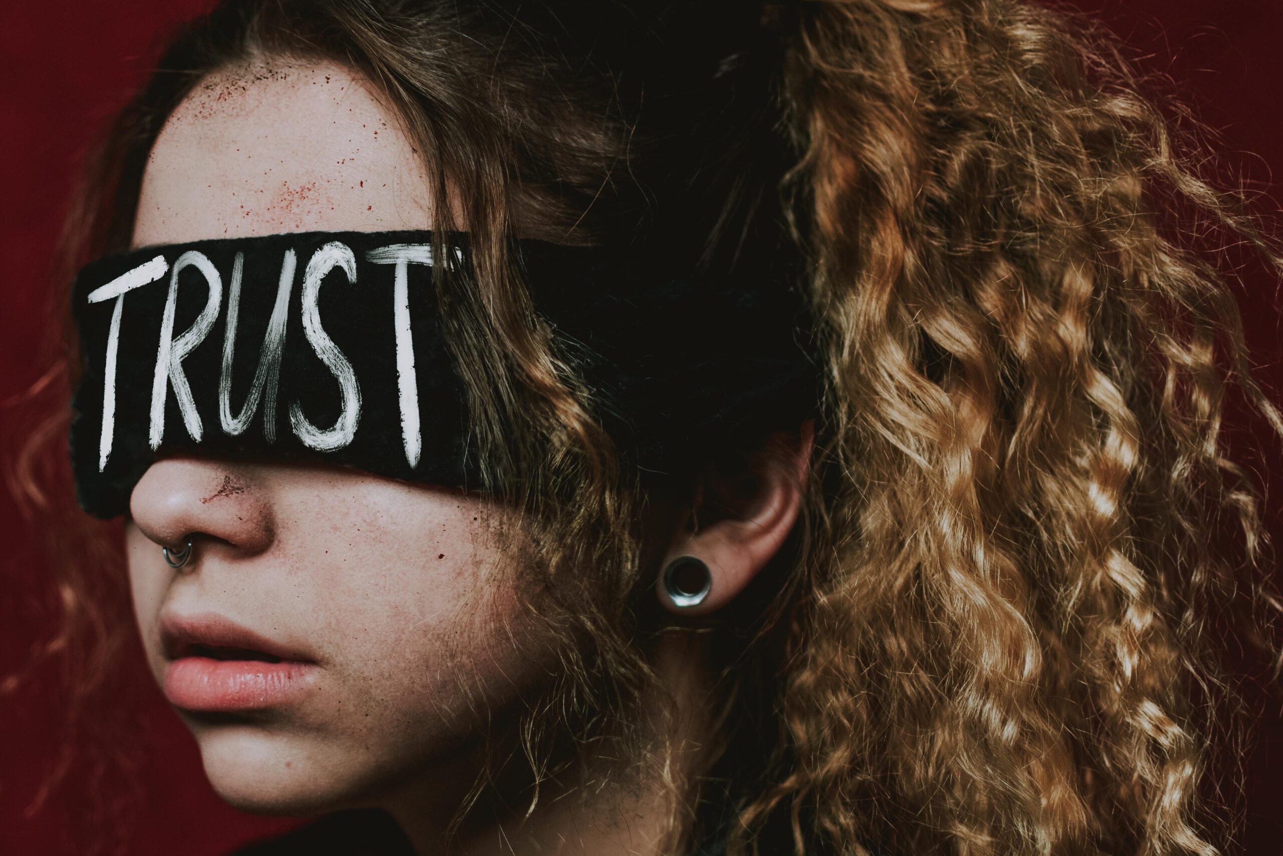 A woman wearing a blindfold with the word 'Trust' against a dark background.