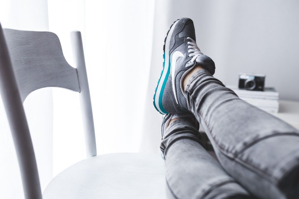 A woman lounging with her feet up on a chair, showcasing grey sneakers. Someone focused on rest and recovery.