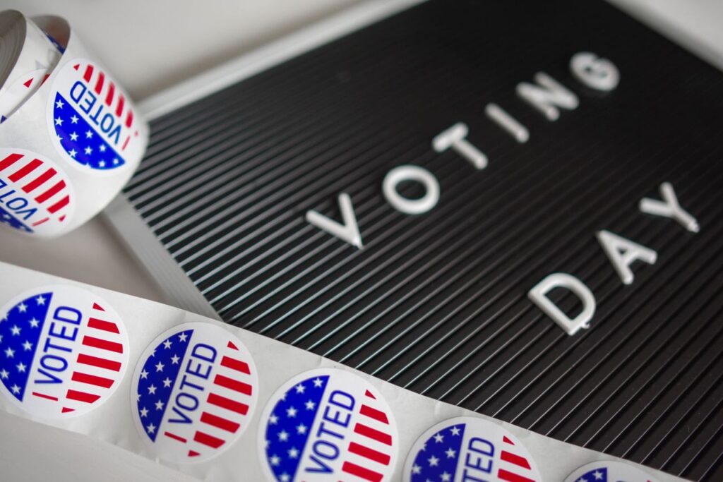 I Voted stickers with an American flag design and Voting Day sign symbolize U.S. electoral participation. Shared as we discuss voting rights.