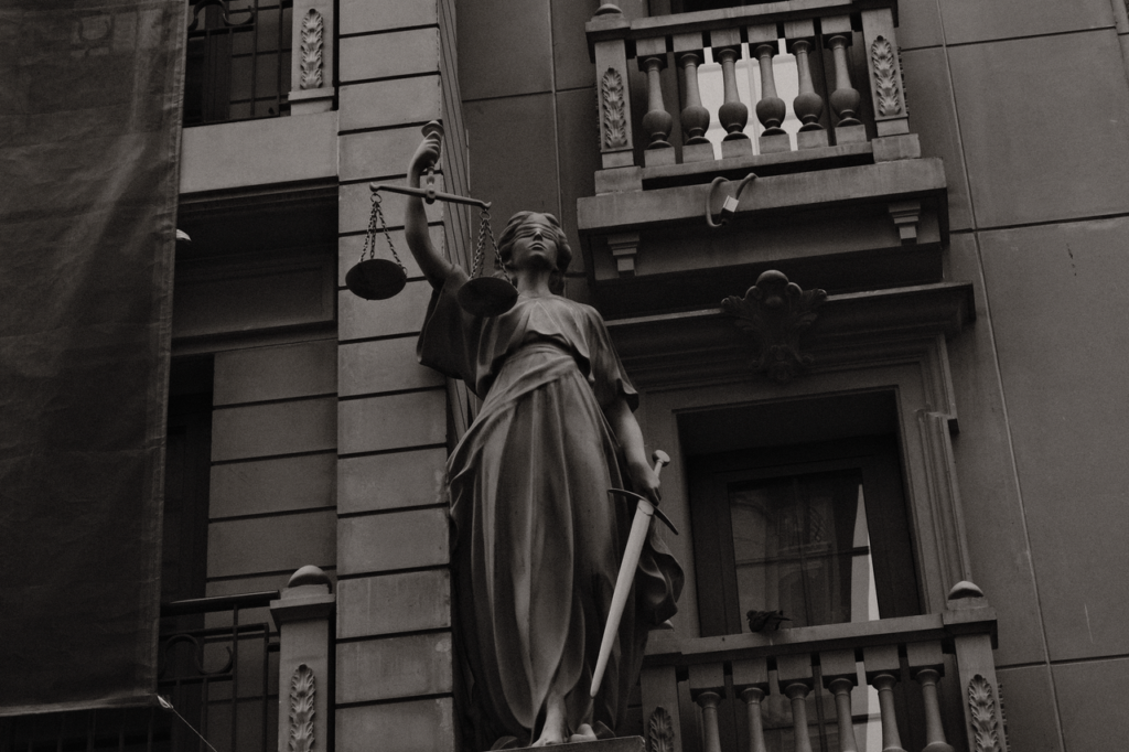A black and white image of Lady Justice statue against a building facade symbolizing law and fairness.