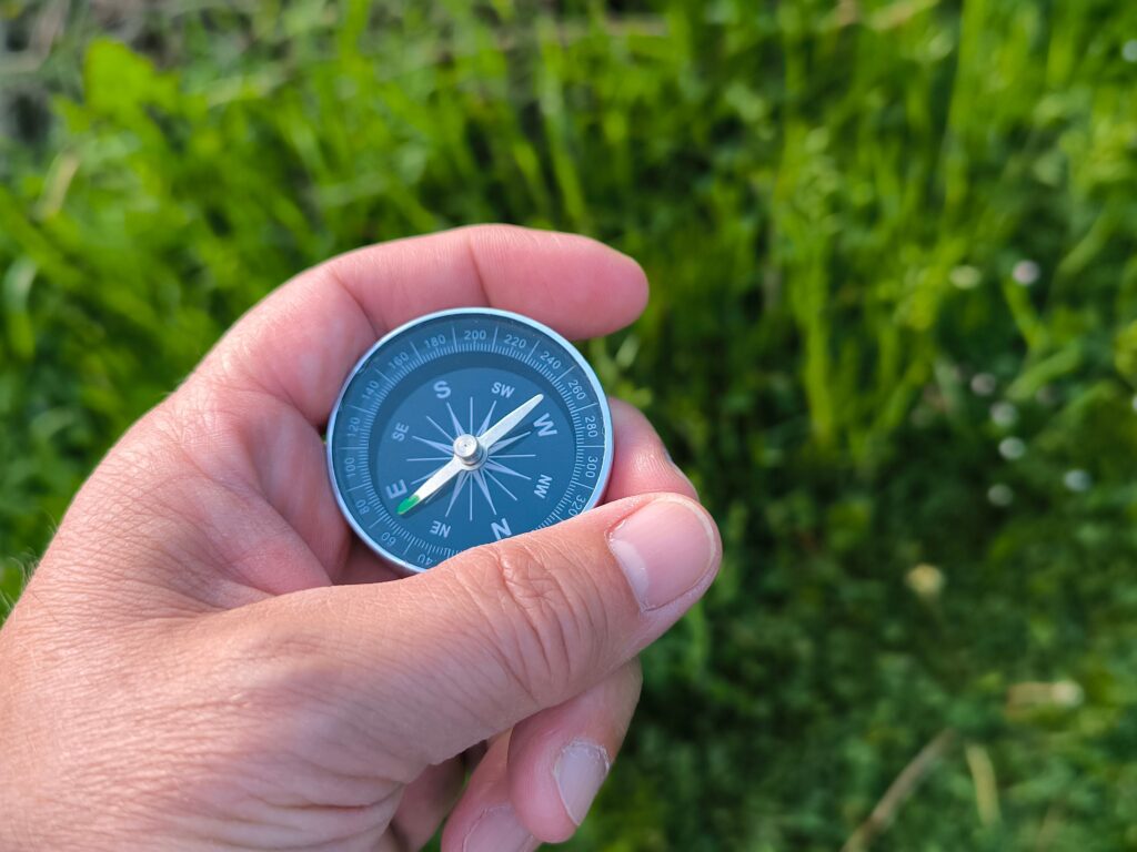 Close-up of a hand holding a compass with a green field in the background.